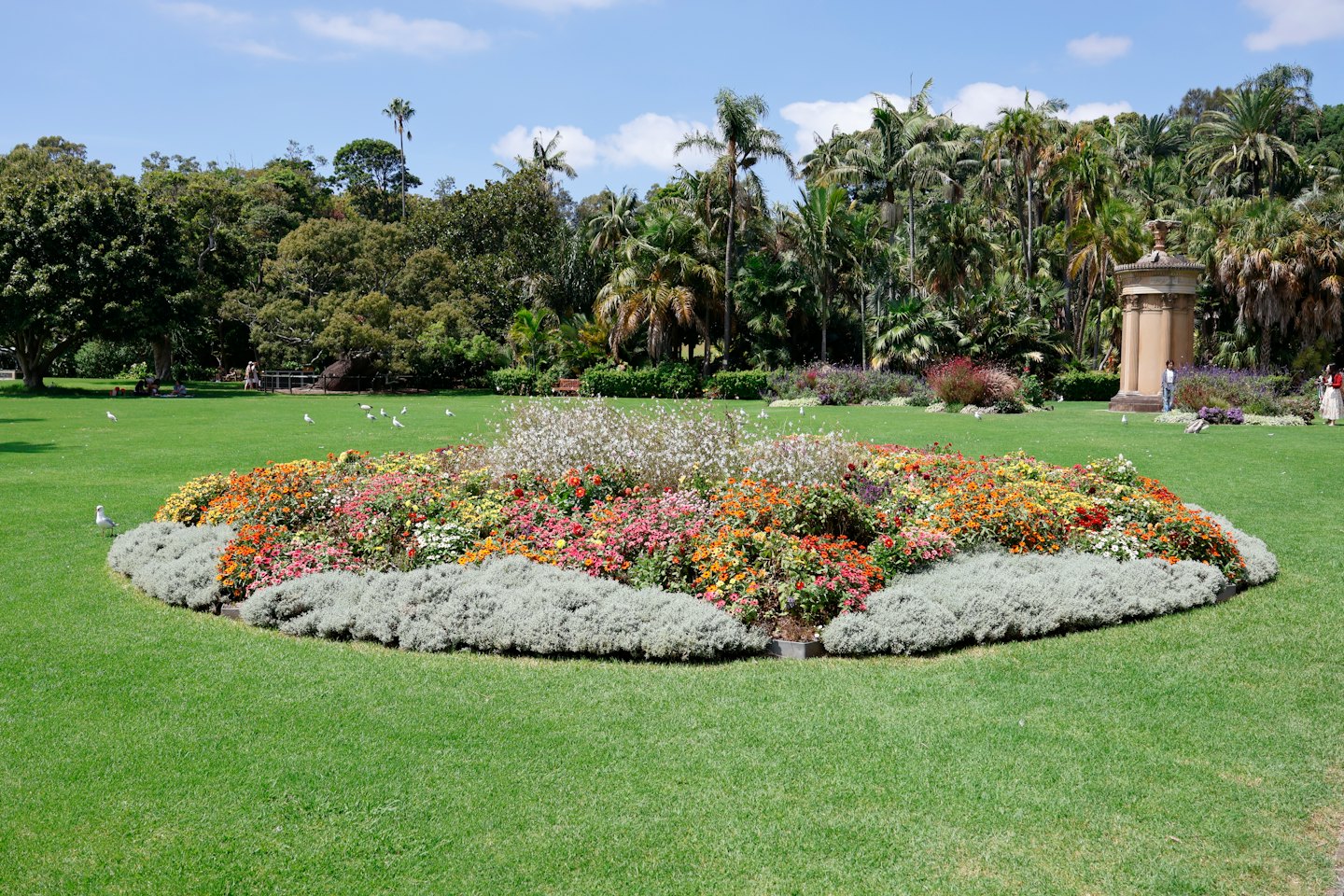 Aiuola fiorita colorata in un parco con alberi e monumento.
